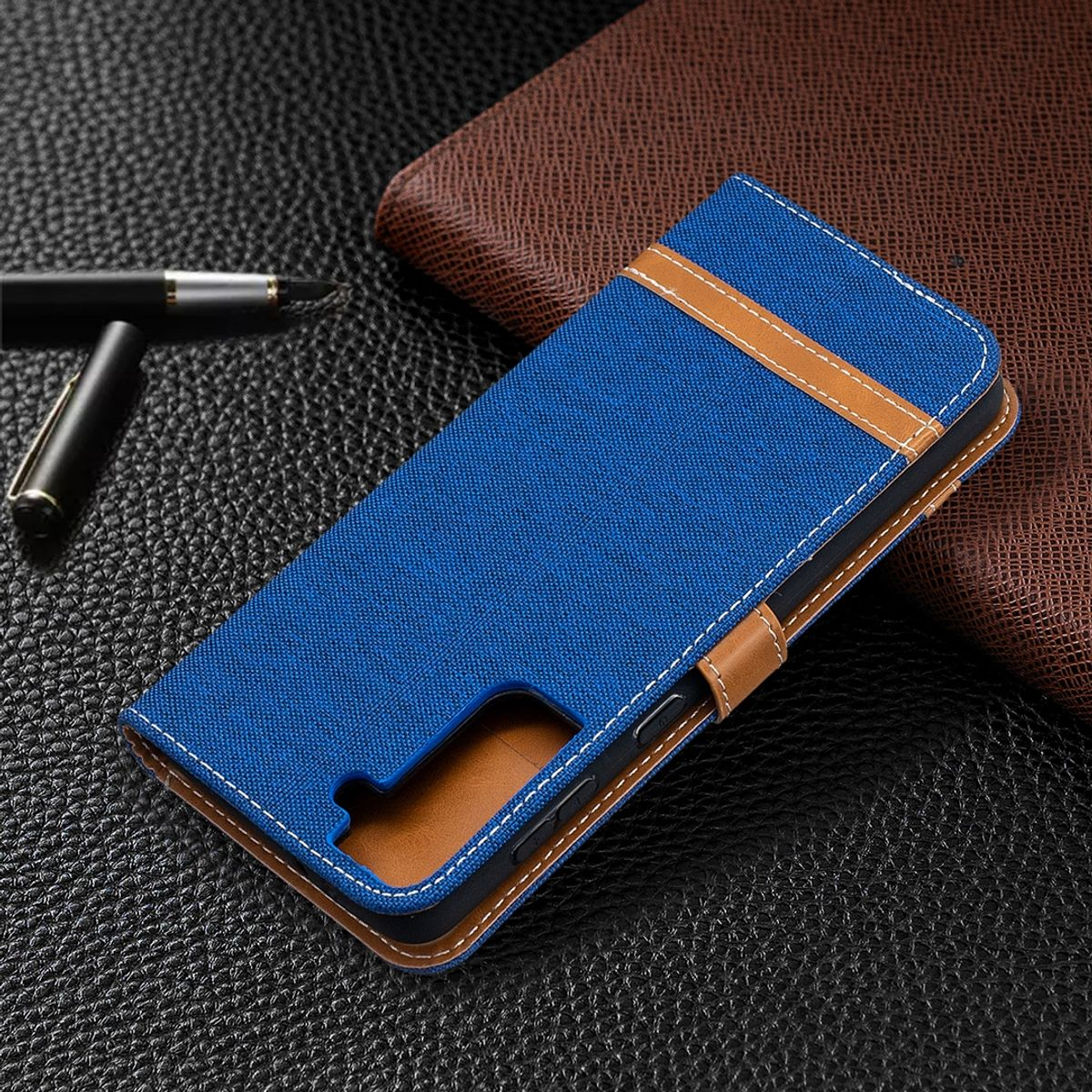 Blaue Handyhülle mit braunen Akzenten. Das Telefon befindet sich in der Hülle, die sich auf einer Lederoberfläche befindet. Ein Stift ist sichtbar.