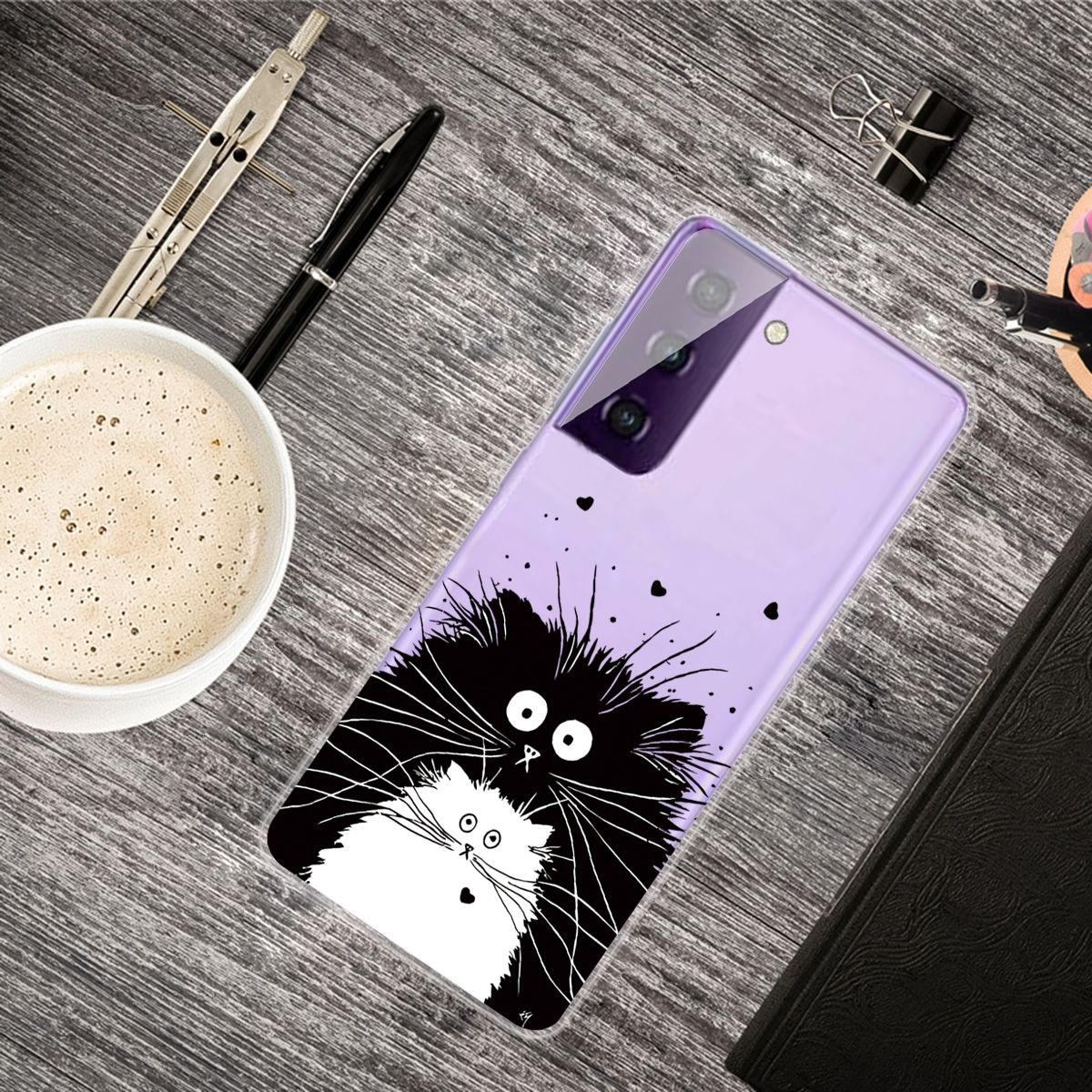Eine Handyhülle mit einer Katzenillustration auf einem Schreibtisch mit Kaffee, Stiften und einem Notizbuch.