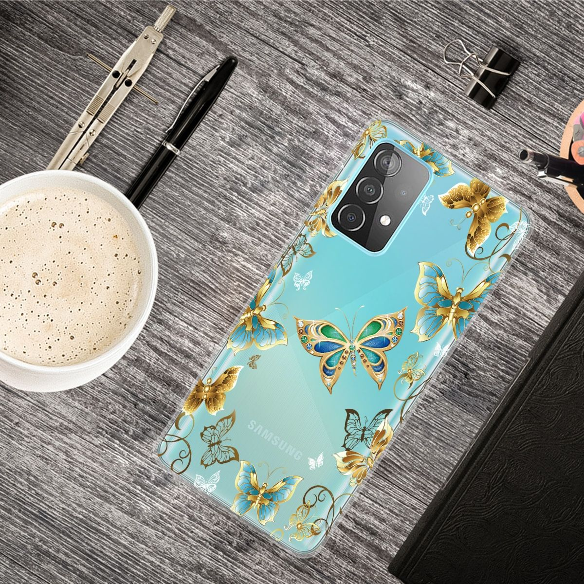 Eine Handyhülle mit Schmetterlingen. Auf dem Tisch stehen eine Kaffeetasse, Stift und Notizbuch.