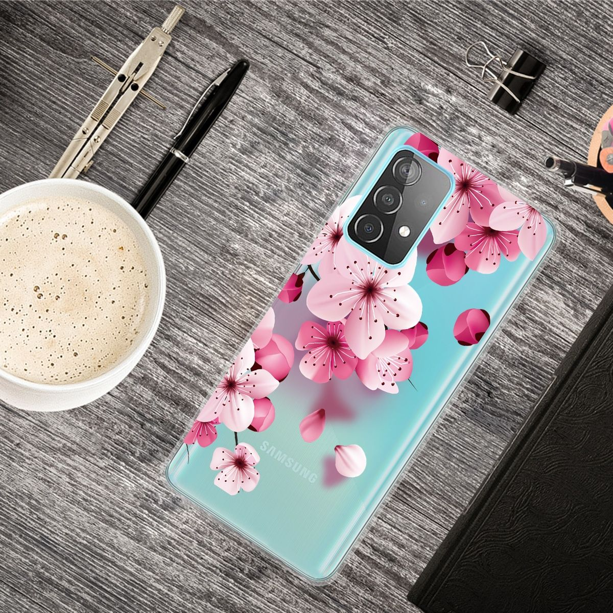 Handyhülle mit Kirschblüten-Design. Hellblaue Hülle mit rosa Blüten. Tasse und Stift liegen daneben.