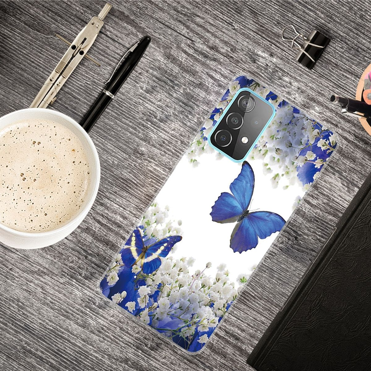 Handyhülle auf einer Holzoberfläche mit Blumen und Schmetterlingen. Es gibt eine Kaffeetasse, einen Stift und eine Büroklammer.
