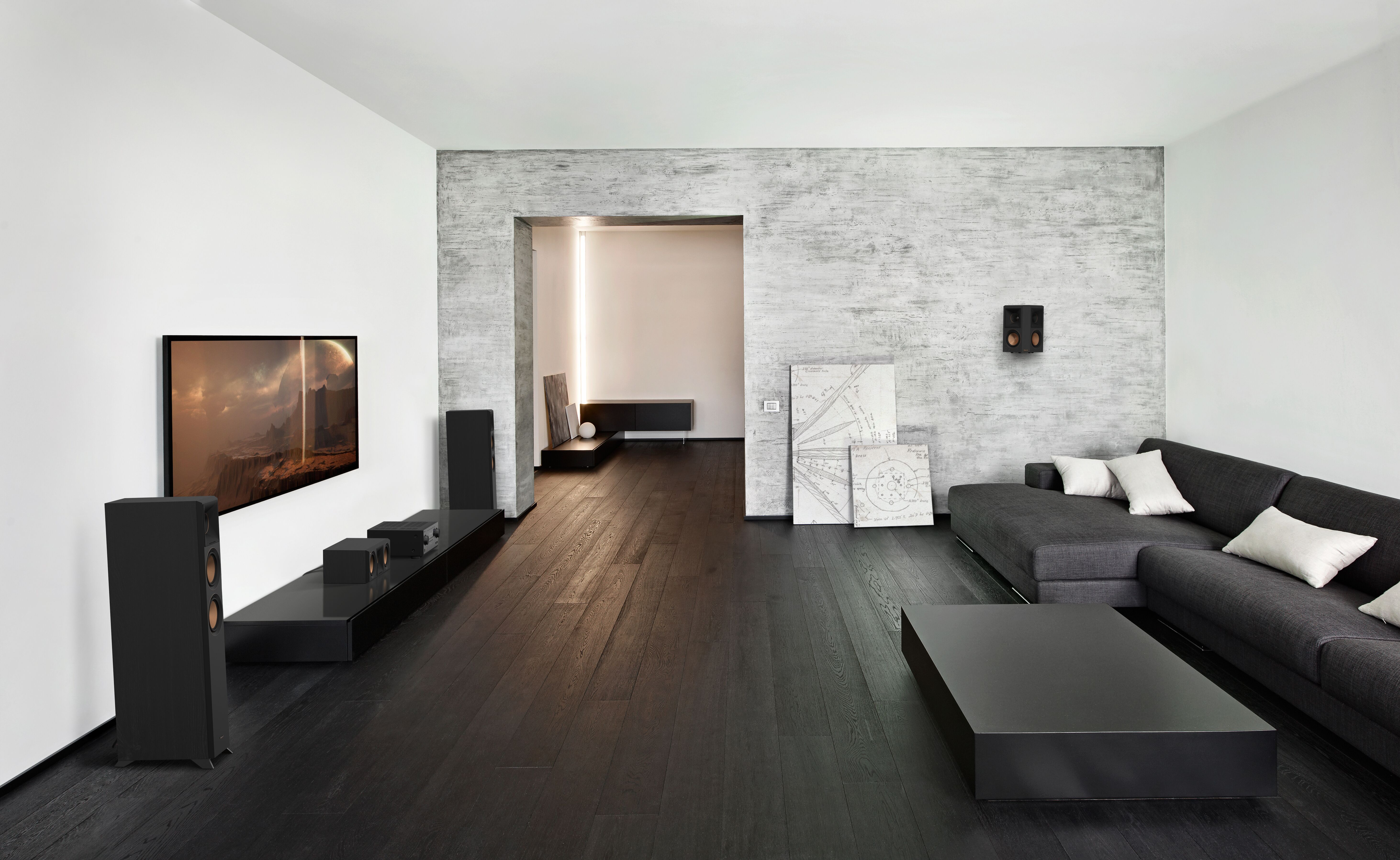 Modernes Wohnzimmer mit dunklem Holzboden, schwarzen Lautsprechern, einem grauen Sofa und einem Fernseher.