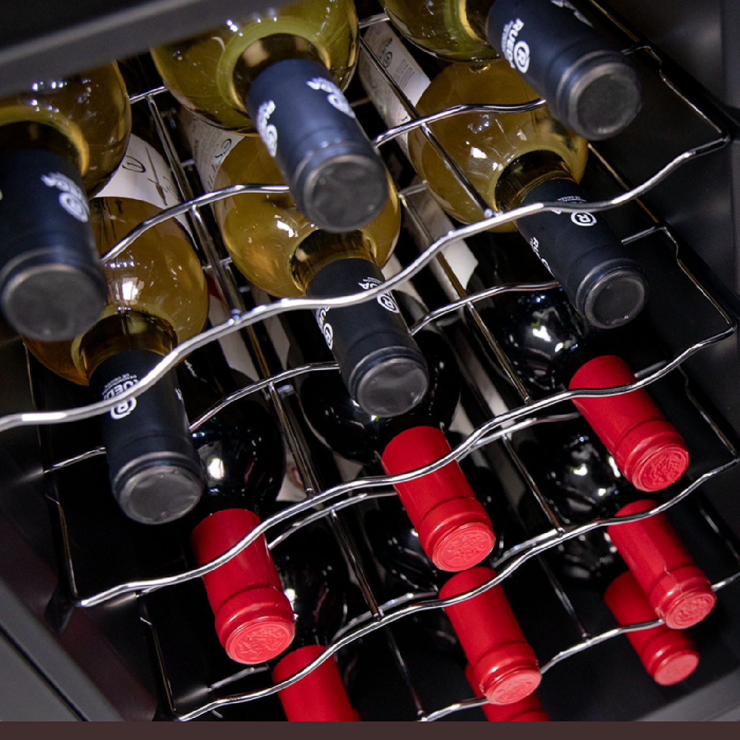 Wine bottles in a wine cooler. Some bottles have black caps, others red.