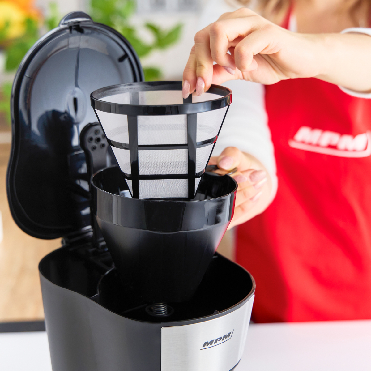 Kobieta wkładająca filtr do ekspresu do kawy. Filtr jest czarno-biały, ekspres czarny.