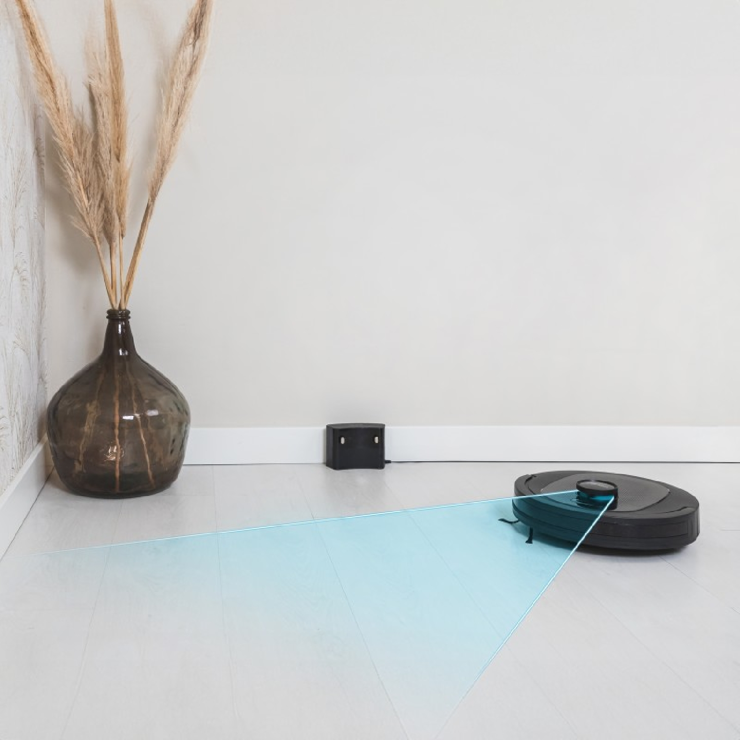 Czarny robot odkurzający sprząta pokój. Po lewej stronie brązowy wazon.