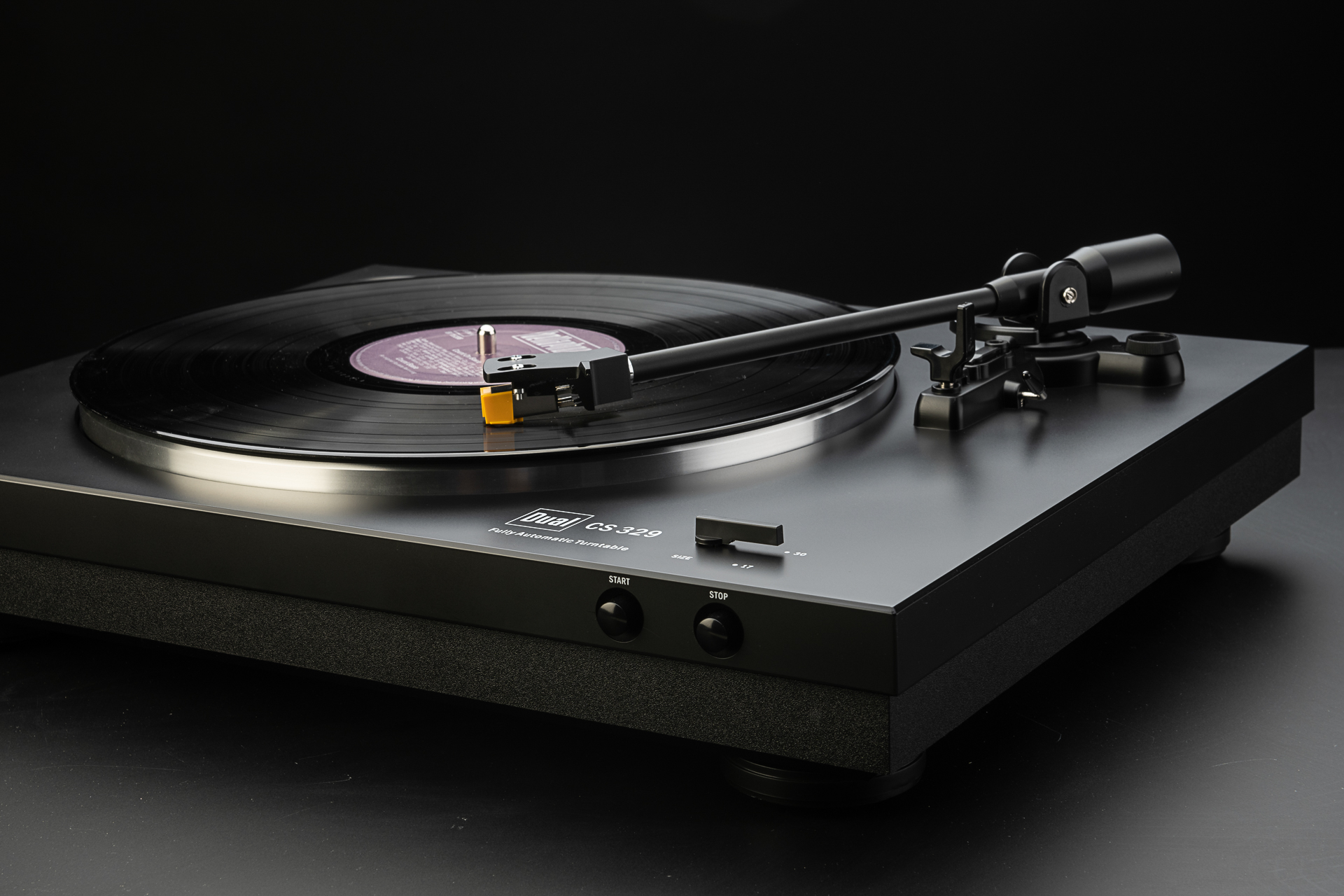 Schwarzer Plattenspieler, Vinyl-Schallplatte spielt. Schwarze Oberfläche. Schräg, dunkler Hintergrund.