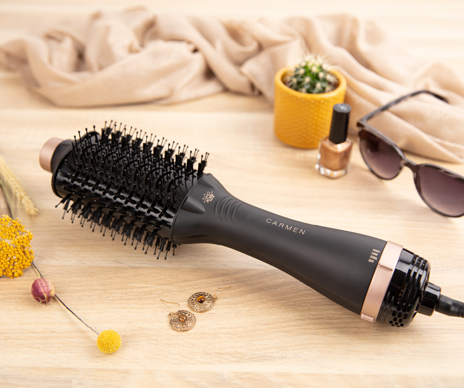 A black curling brush and accessories on a wooden surface. The brand is Carmen.
