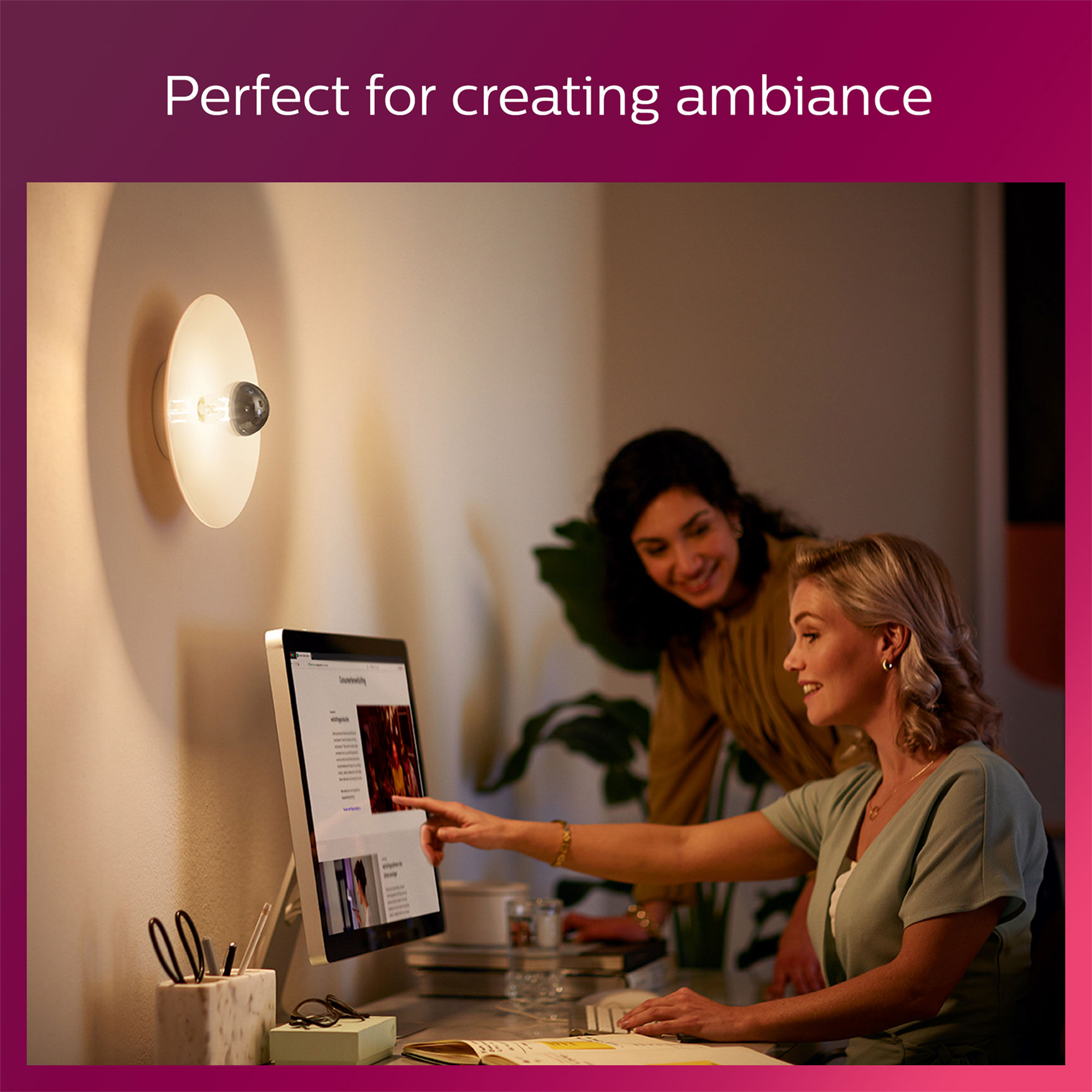 Zwei Frauen betrachten einen Computerbildschirm, mit einer modernen Lampe an der Wand.