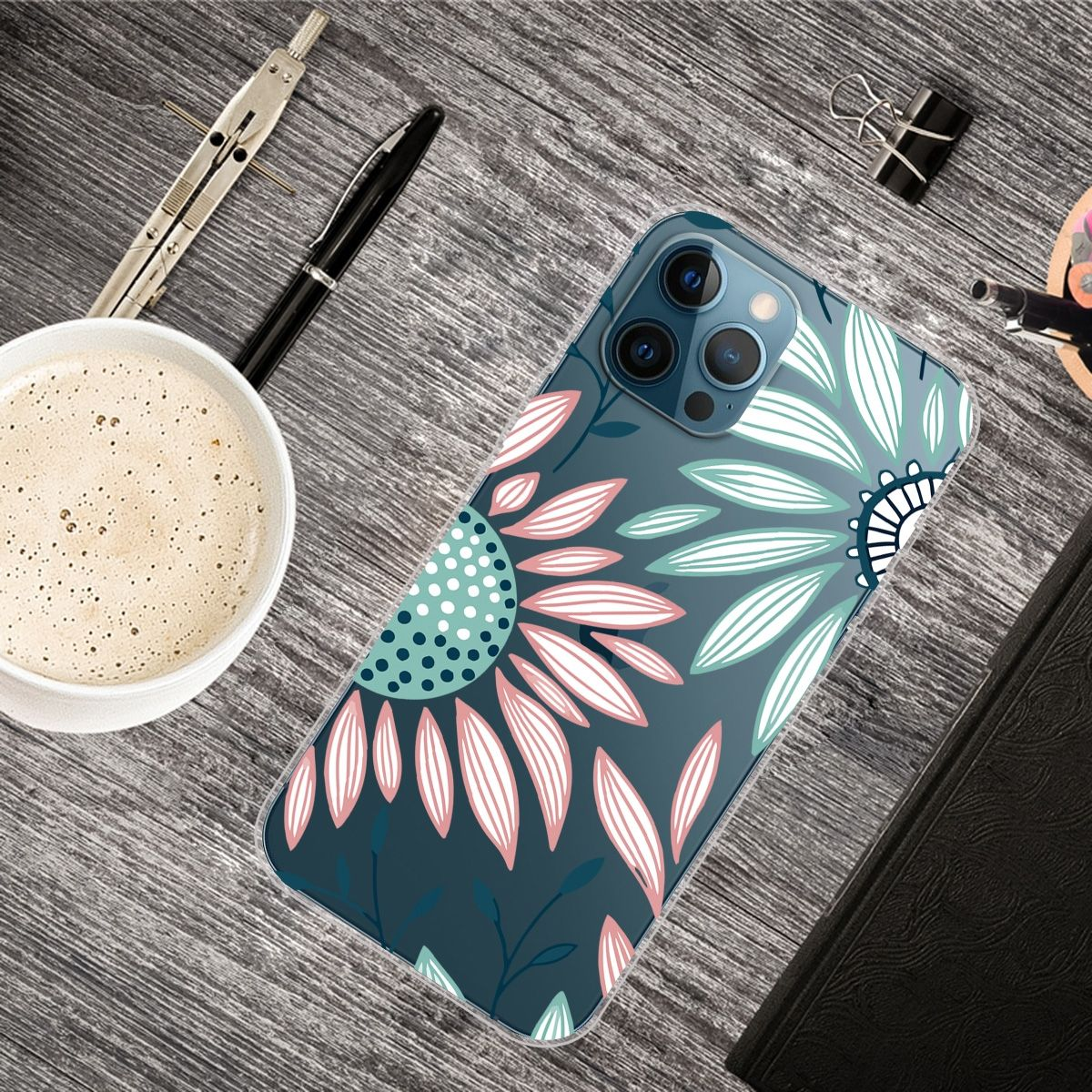 Ein Telefon mit floraler Hülle liegt auf einem Holztisch. Eine Kaffeetasse, Stift und andere Gegenstände sind dabei.