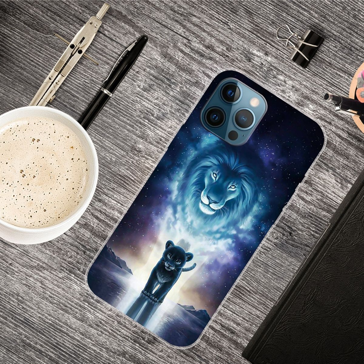 Handyhülle mit Löwenbild, neben Kaffee, Stiften und einem Notizblock.