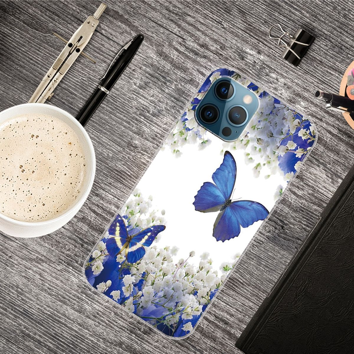 Handyhülle mit Schmetterlingen und Blumen auf einem Schreibtisch mit Kaffee und Stiften.