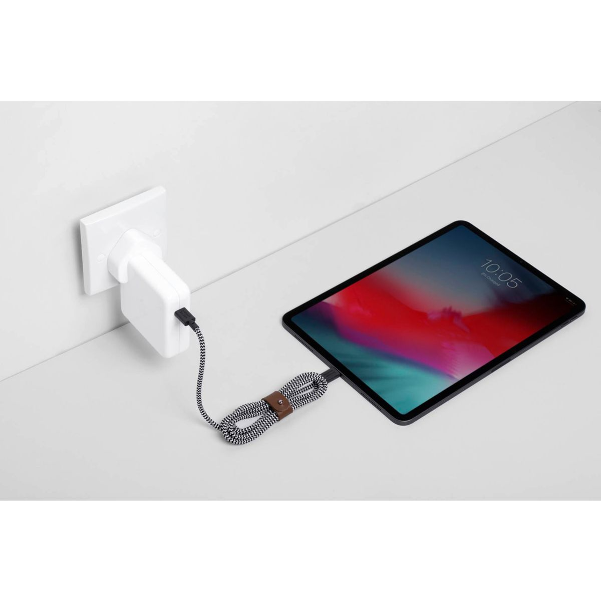 Tablet wird mit einem weißen Stecker und einem schwarz-weißen Kabel aufgeladen. Das Tablet hat ein rotes und lila Farbverlaufstapete.