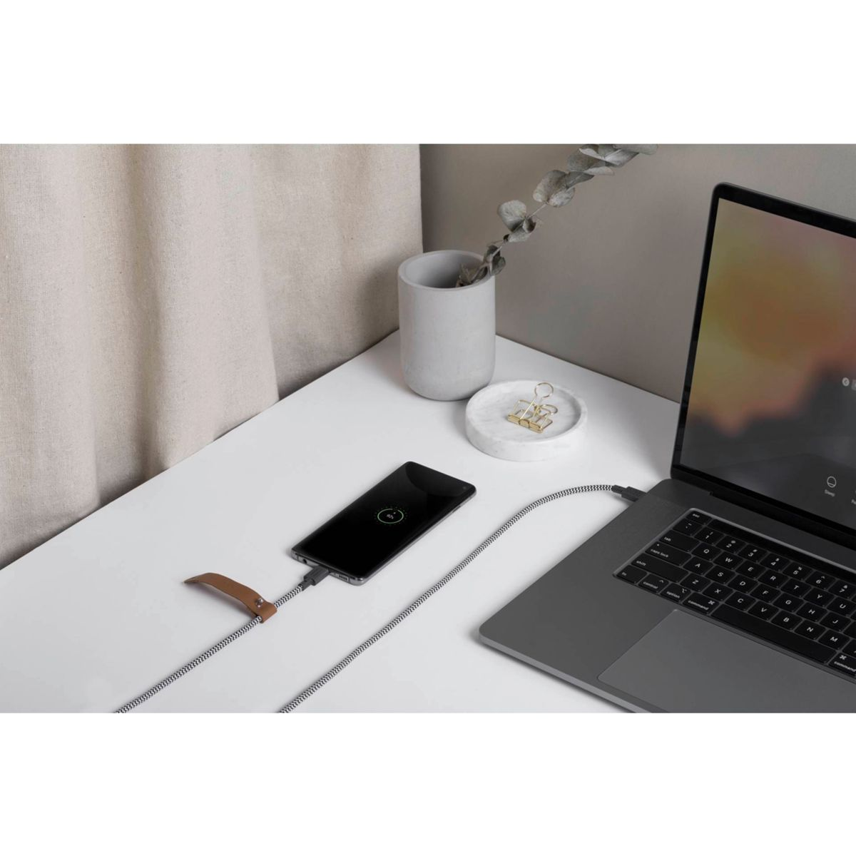 Smartphone lädt auf weißem Schreibtisch neben Laptop und Zubehör.