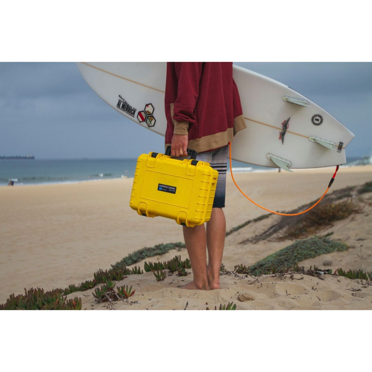 Mann mit gelber wasserdichter Box und Surfbrett am Strand. Sonniger Tag.