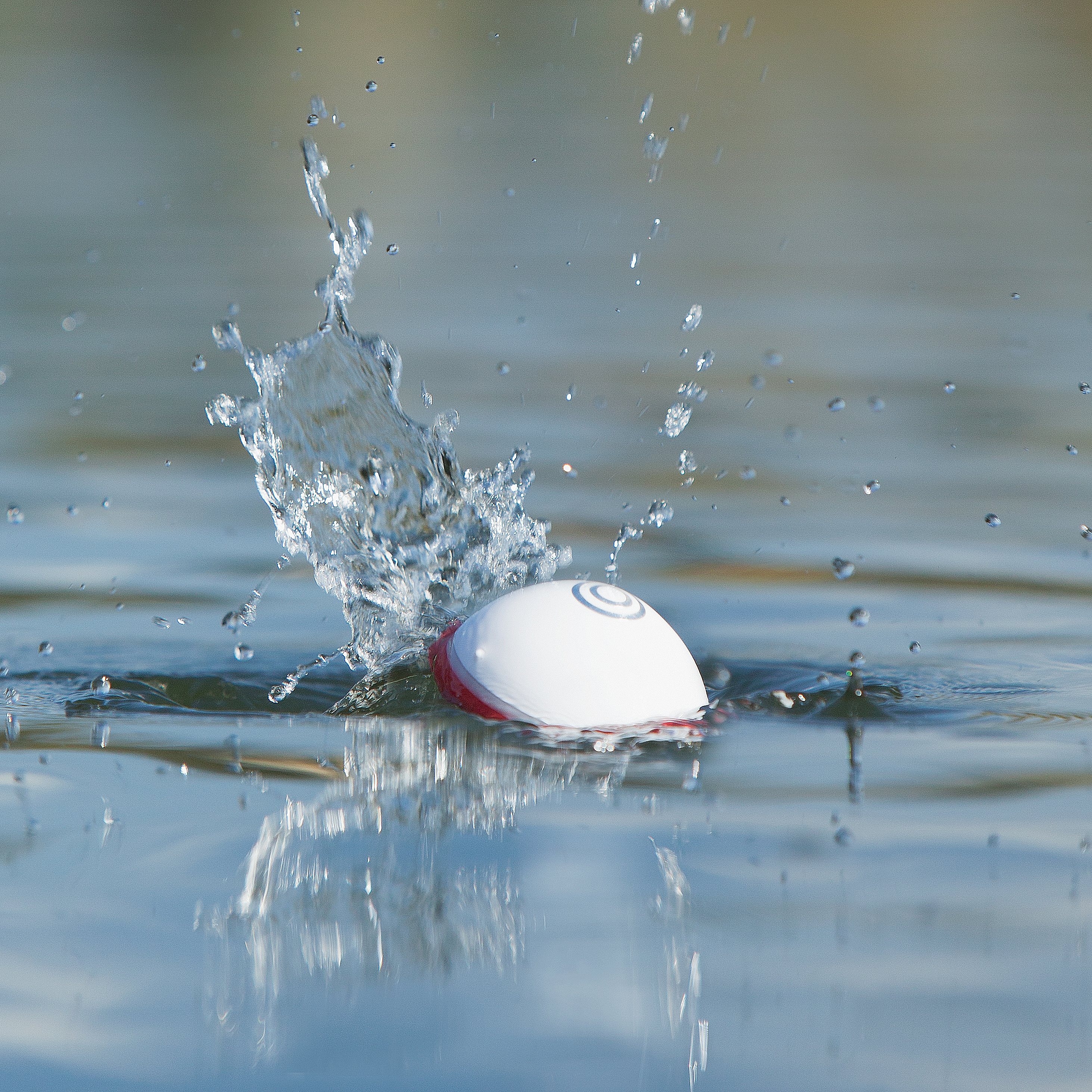 Ein weiß-roter Ball, der ins Wasser spritzt und eine Welle erzeugt.