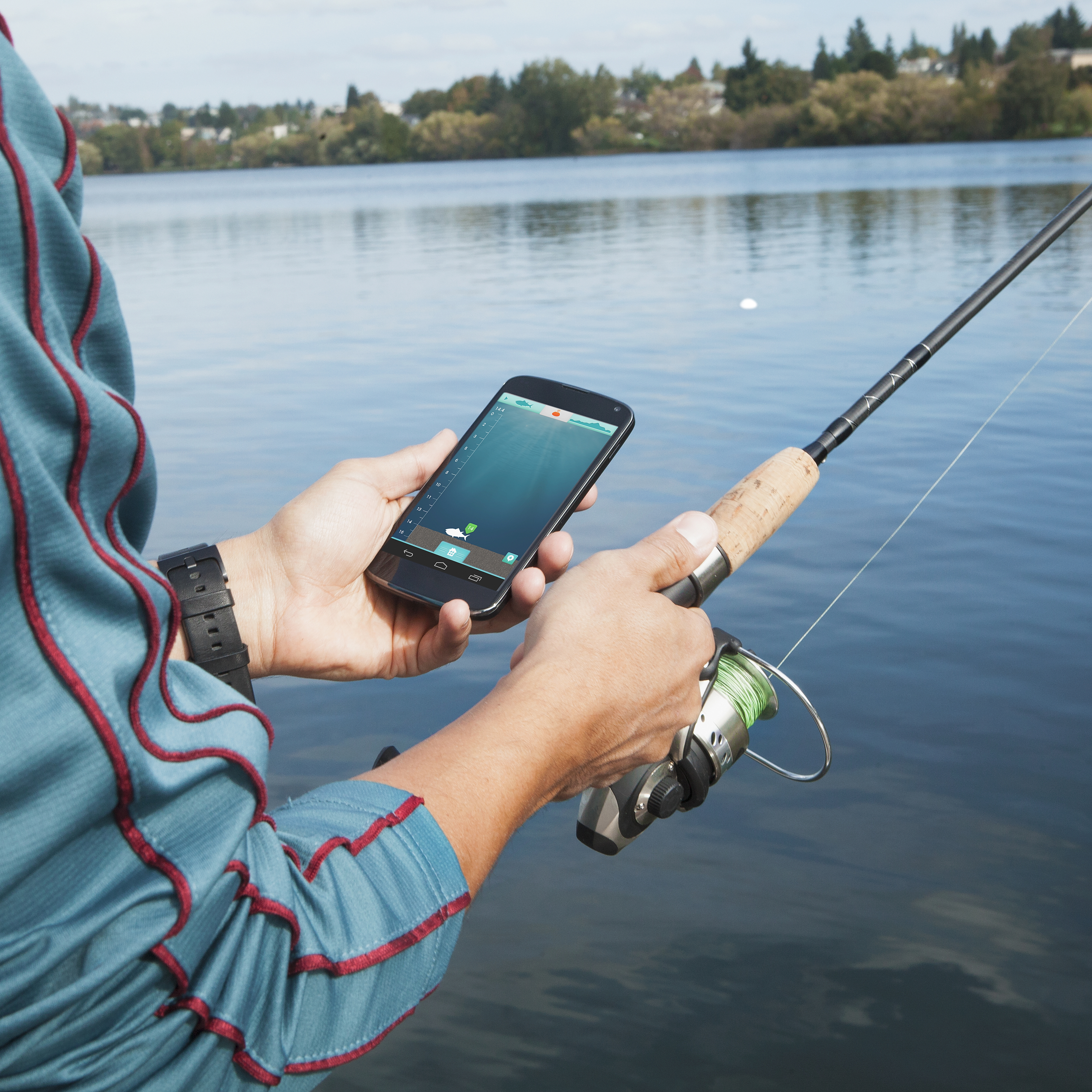 Person angelt, hält Telefon mit Fischfinder-App. See im Hintergrund.