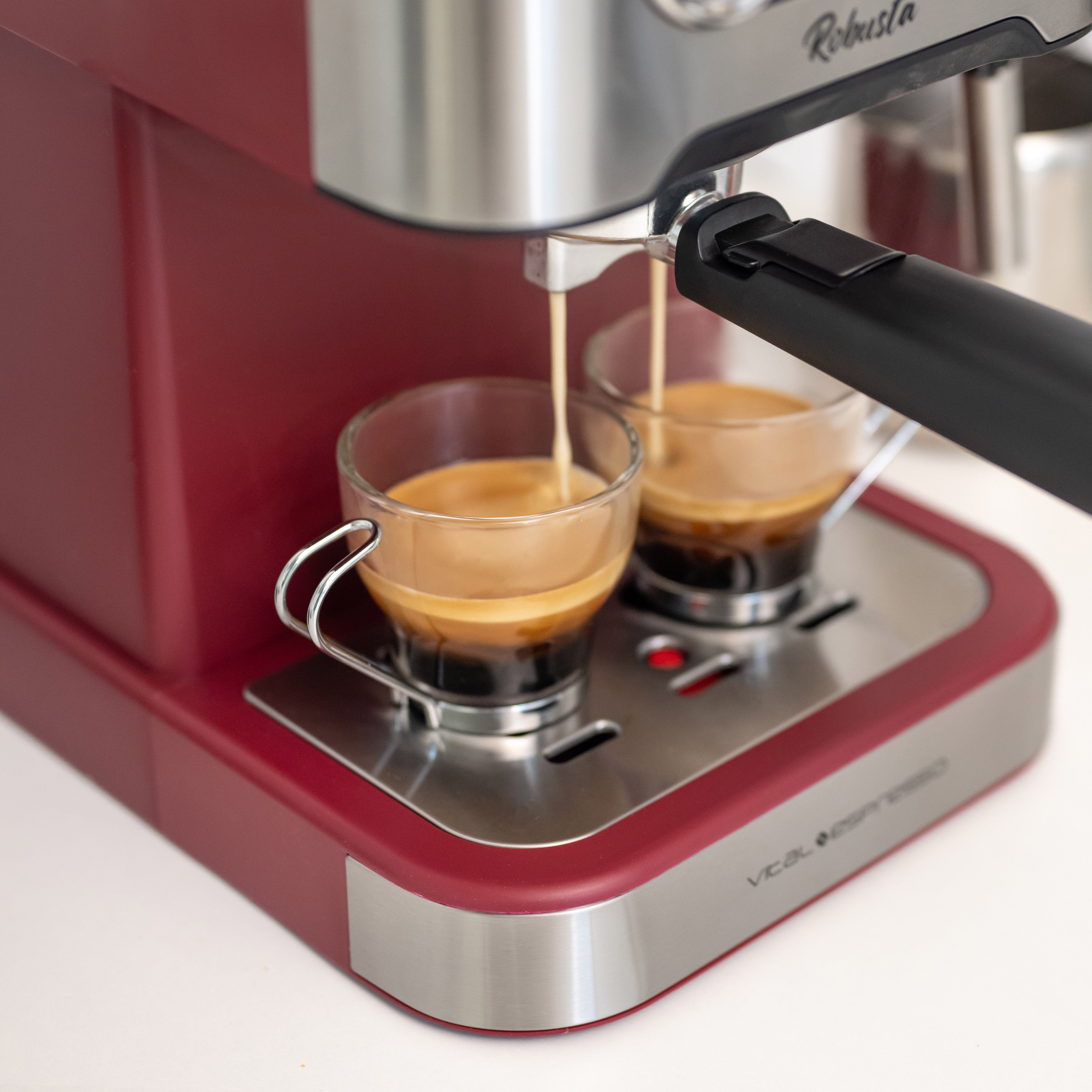 Máquina de espresso dispensando café en dos tazas de cristal.