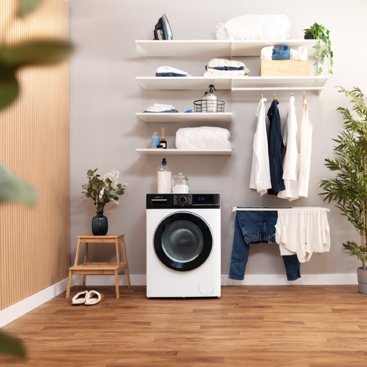 Pralka z białą pralką i suszarką, półkami i wiszącymi ubraniami. Drewniana podłoga.