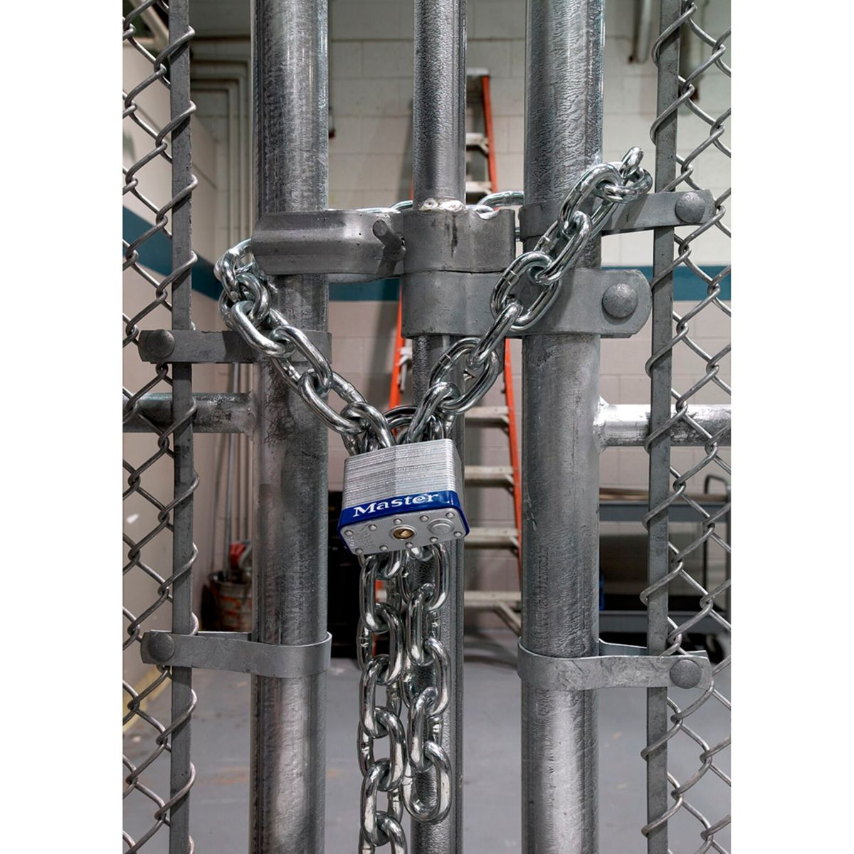 Ein silbernes Metalltor, das mit einer Kette und einem Schloss verschlossen ist. Eine Leiter ist im Hintergrund.