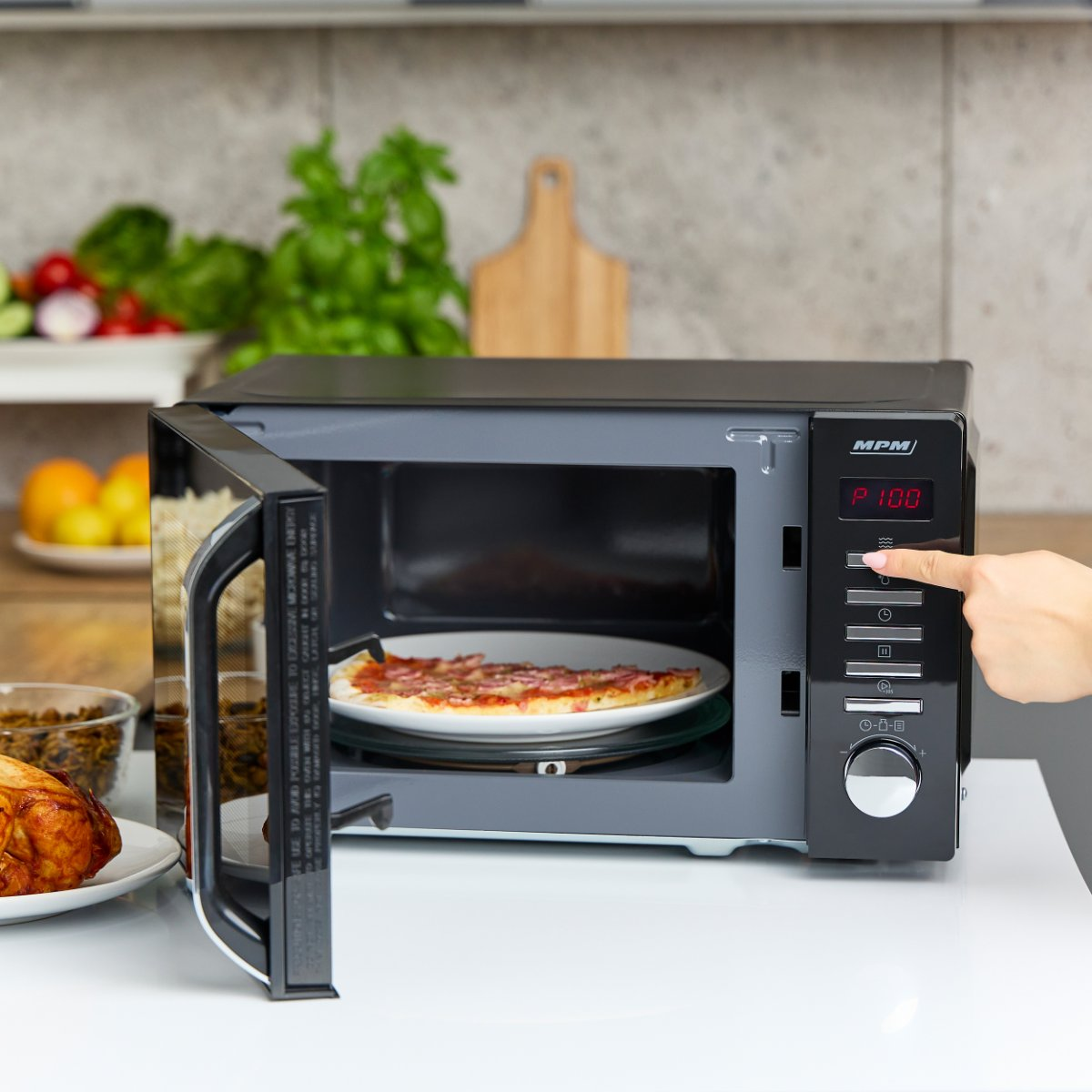 Mikrofalówka z kawałkiem pizzy na talerzu. Drzwi otwarte. Ręka dotyka panelu.