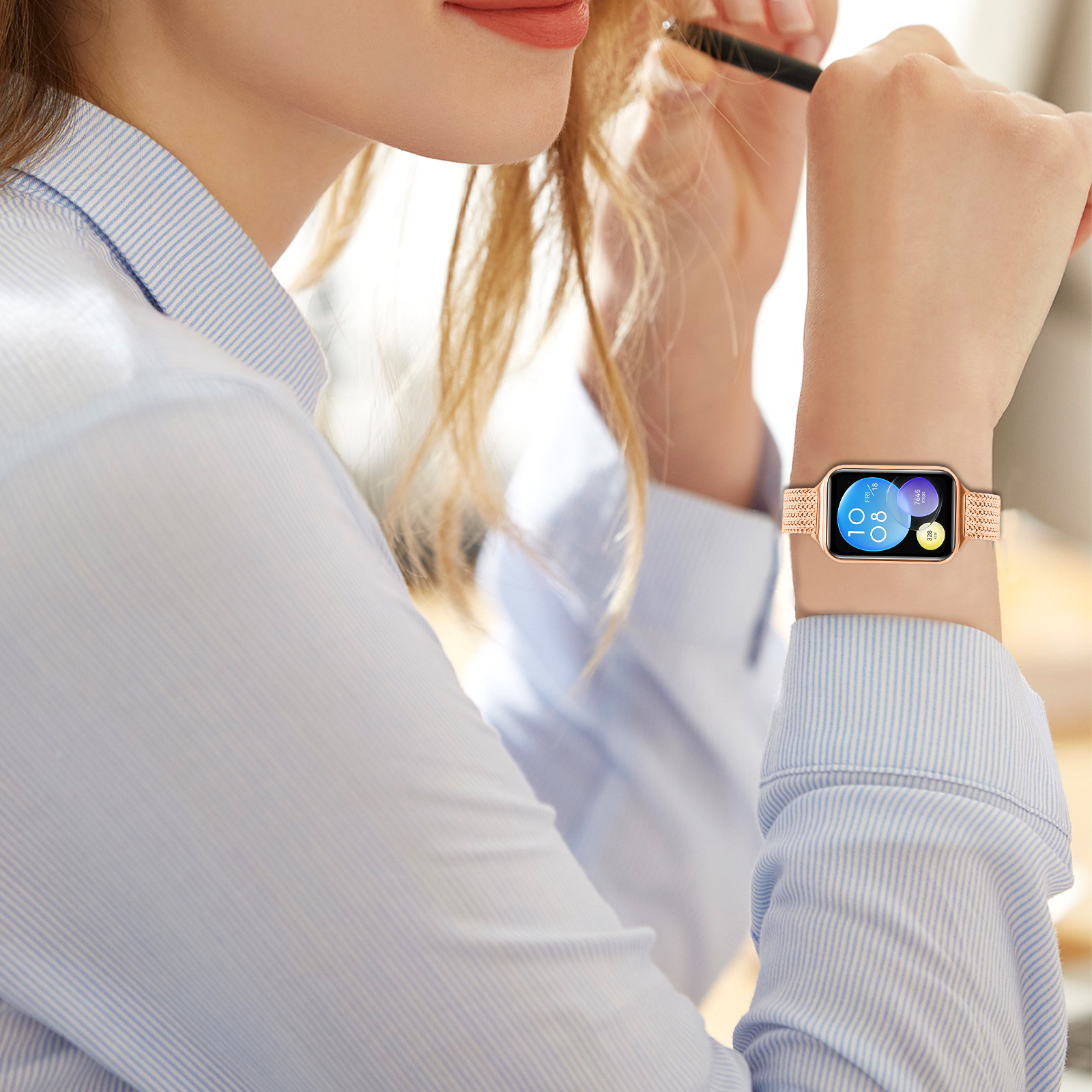 Das Handgelenk einer Frau mit einer Smartwatch in Roségold. Sie hält einen Make-up-Pinsel.