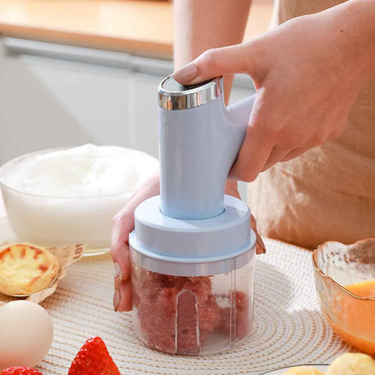 Person vermischt Lebensmittel mit einem blauen Handmixer, Zutaten und Schüsseln daneben.