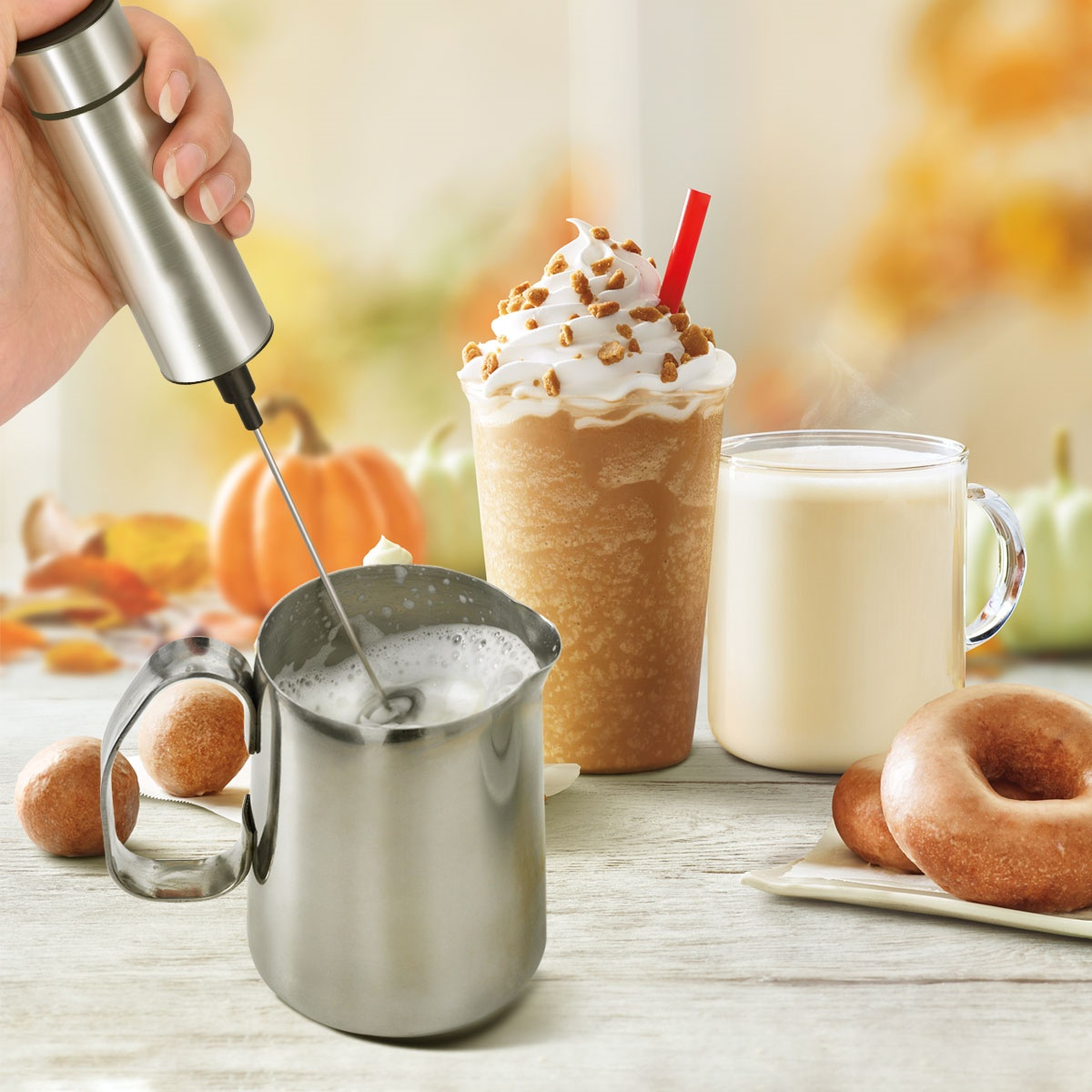 Milchaufschäumer aus Edelstahl in Gebrauch. Milch für Getränke aufschäumen, mit Getränken und Donuts.
