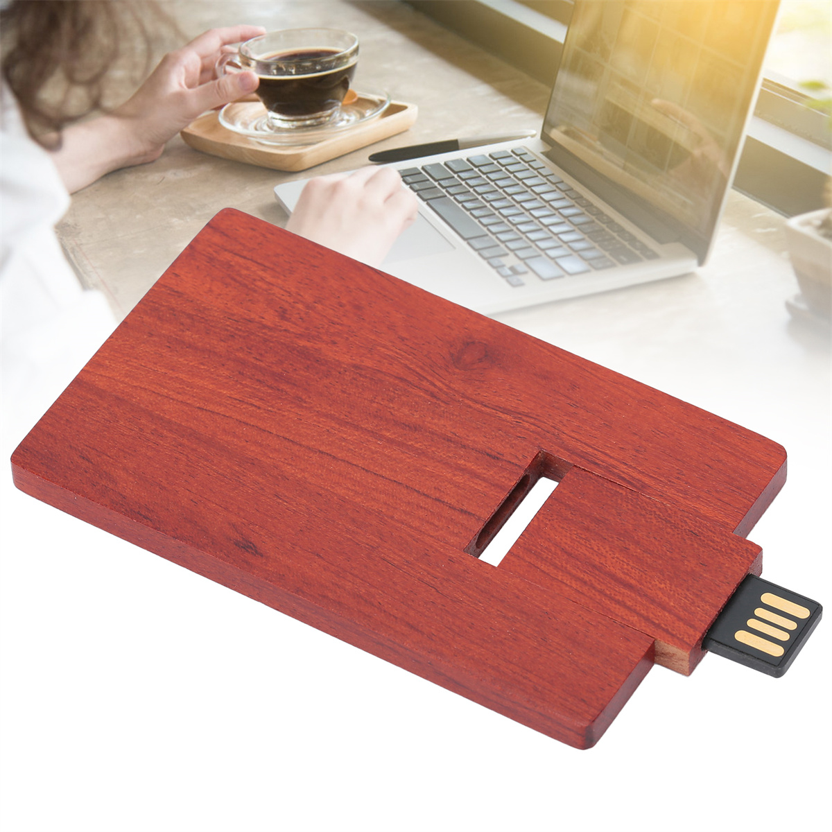 Ein USB-Stick aus Holz liegt auf einem Tisch, im Hintergrund ein Laptop und Kaffee.