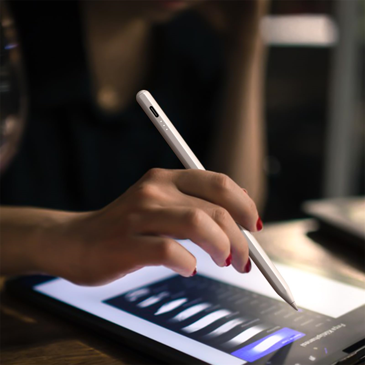 Eine Hand, die einen weißen Stift auf einem Tablet verwendet. Der Hintergrund ist verschwommen, mit rotem Nagellack.
