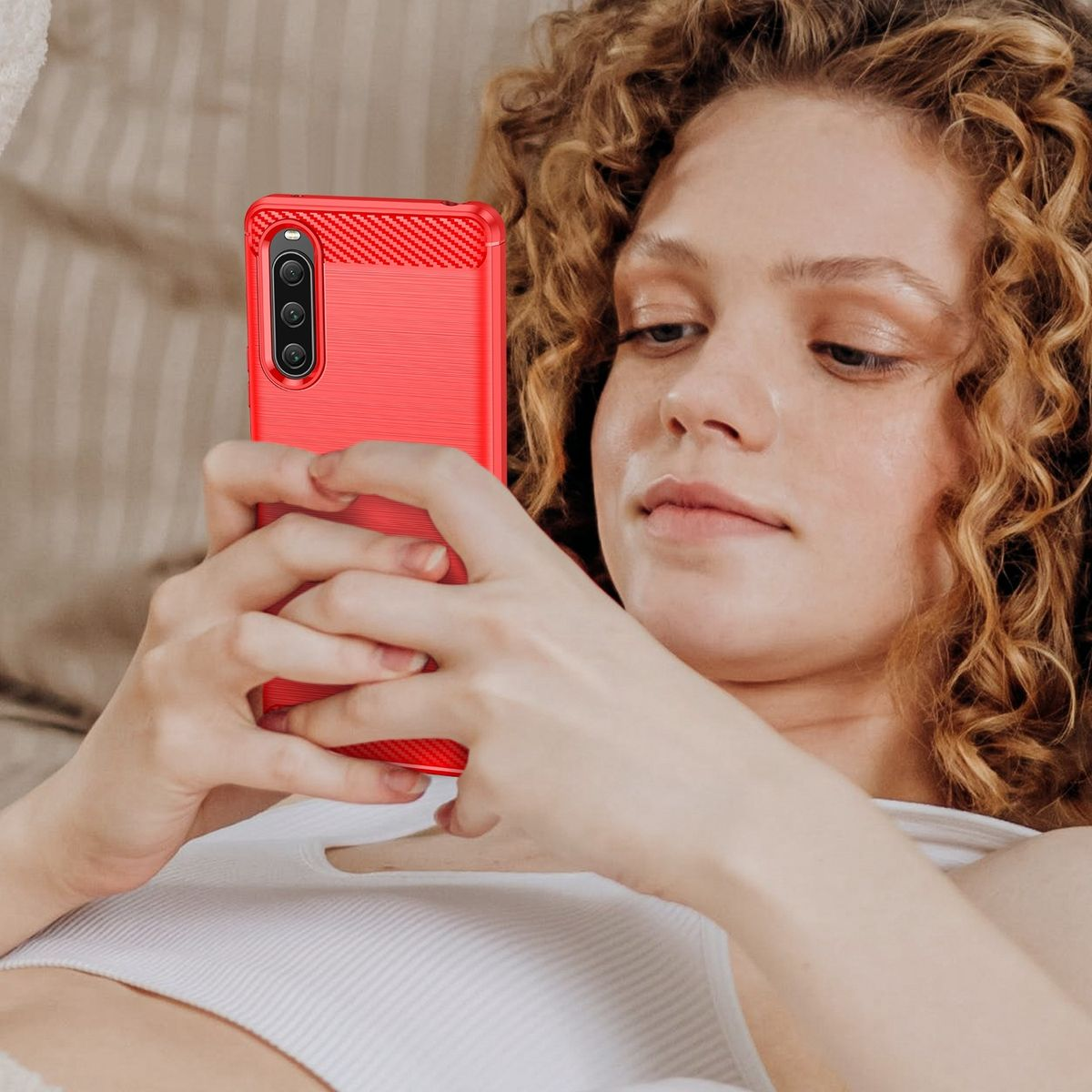 Frau hält eine rote Handyhülle. Sie schaut auf das Telefon. Das Telefon ist im Fokus.