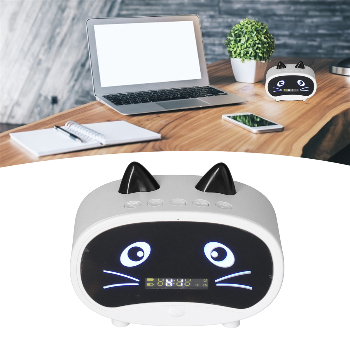 Ein katzenförmiger Lautsprecher mit digitaler Anzeige. Ein Laptop und ein Telefon stehen auf dem Holztisch.