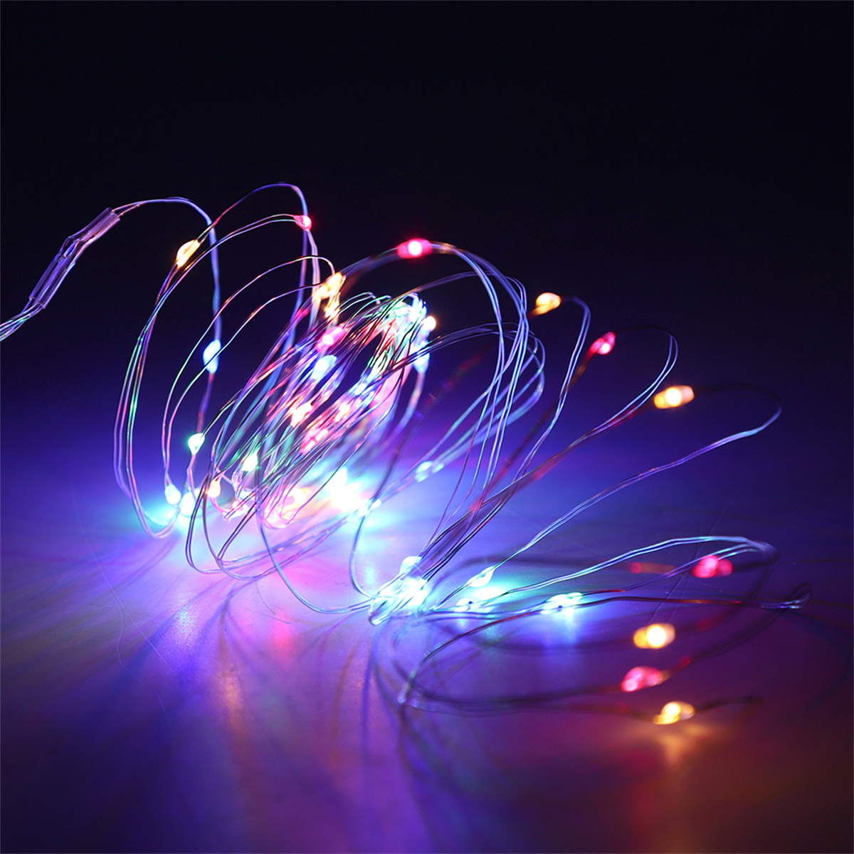 Lichterkette mit vielen kleinen bunten LEDs auf dünnen silbernen Drähten. Sie liegen auf dunklem Untergrund.