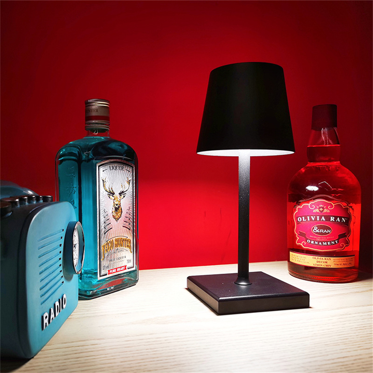 Eine Tischlampe mit schwarzem Lampenschirm und Sockel. Dahinter stehen zwei Flaschen. Links steht ein Vintage-Radio.