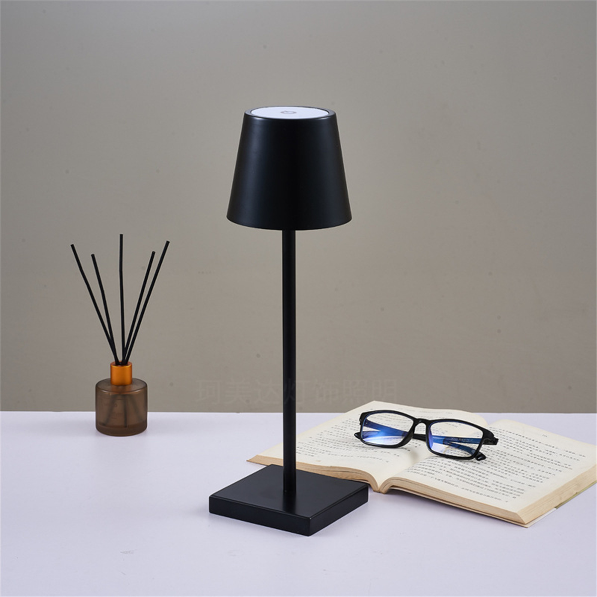 Schwarze Tischlampe mit schlichtem Design. Sie steht auf einer weißen Oberfläche mit einem Buch und einer Brille.