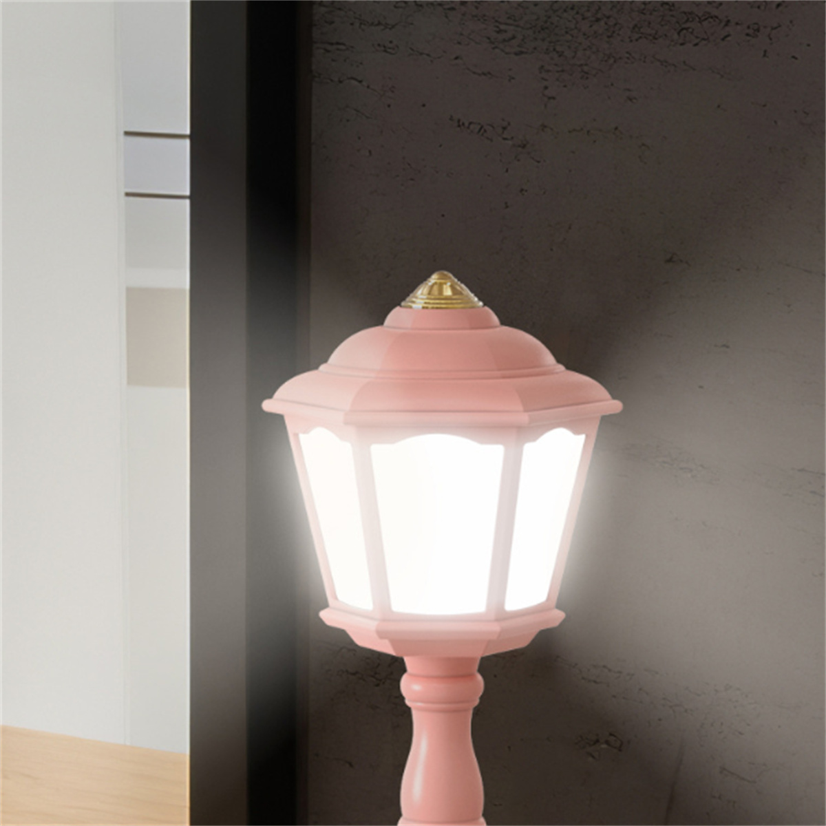 Rosa Straßenlaterne, beleuchtet, mit weißem Licht, vor dunkelgrauer Wand.