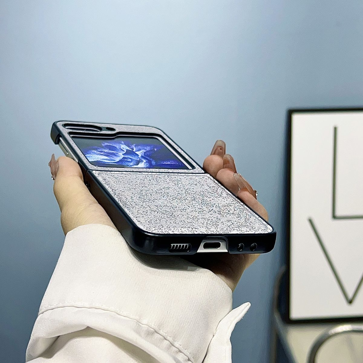 Die Hand einer Person, die eine geschlossene, gefaltete Smartphone-Hülle mit silberner Textur hält.