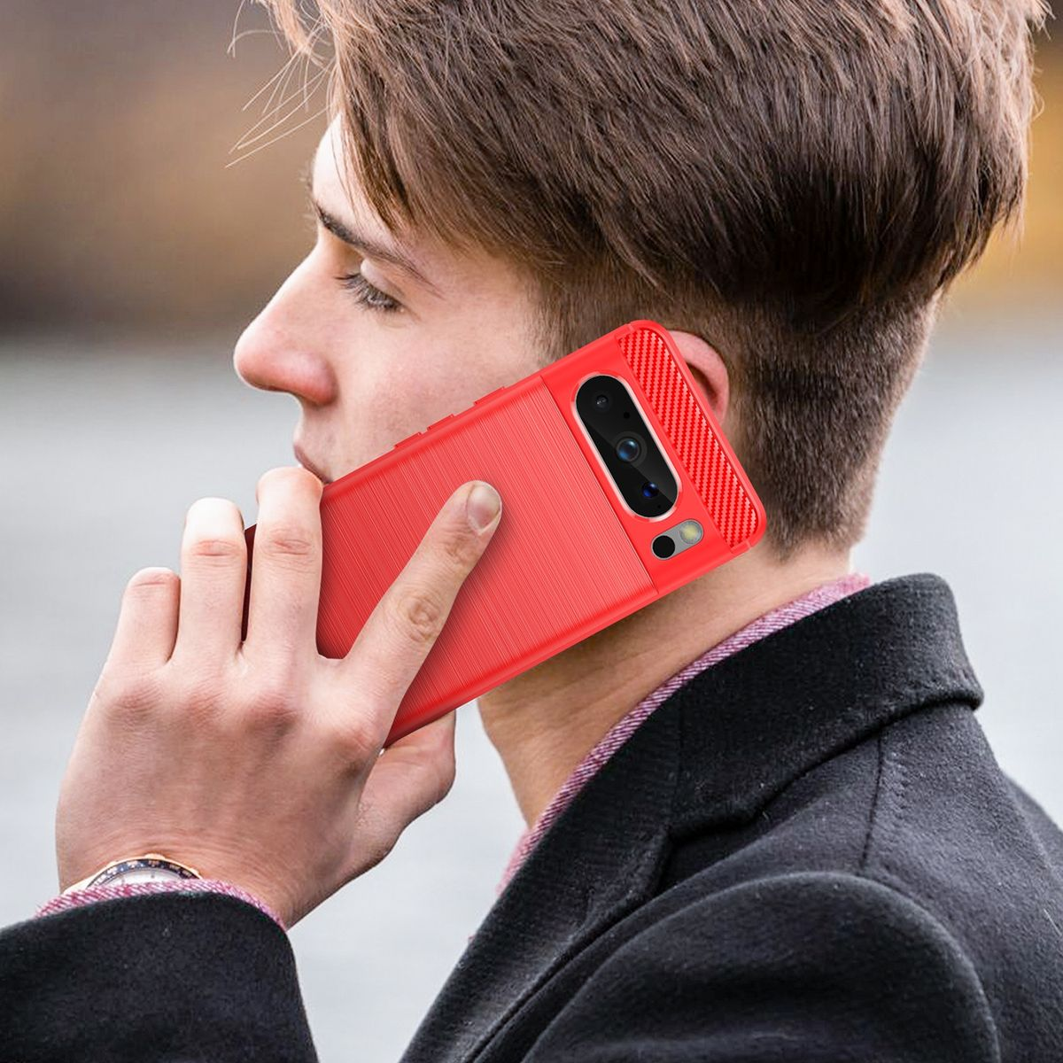 Ein Mann hält ein rotes Telefon an sein Ohr. Er trägt einen schwarzen Mantel, mit verschwommenem Hintergrund.