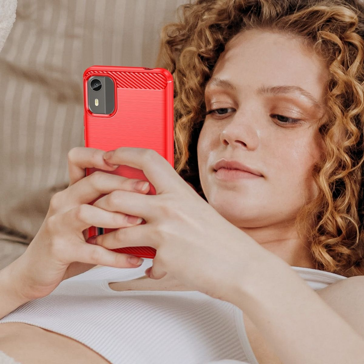 Frau mit lockigem Haar hält eine rote Handyhülle. Sie schaut auf das Telefon.