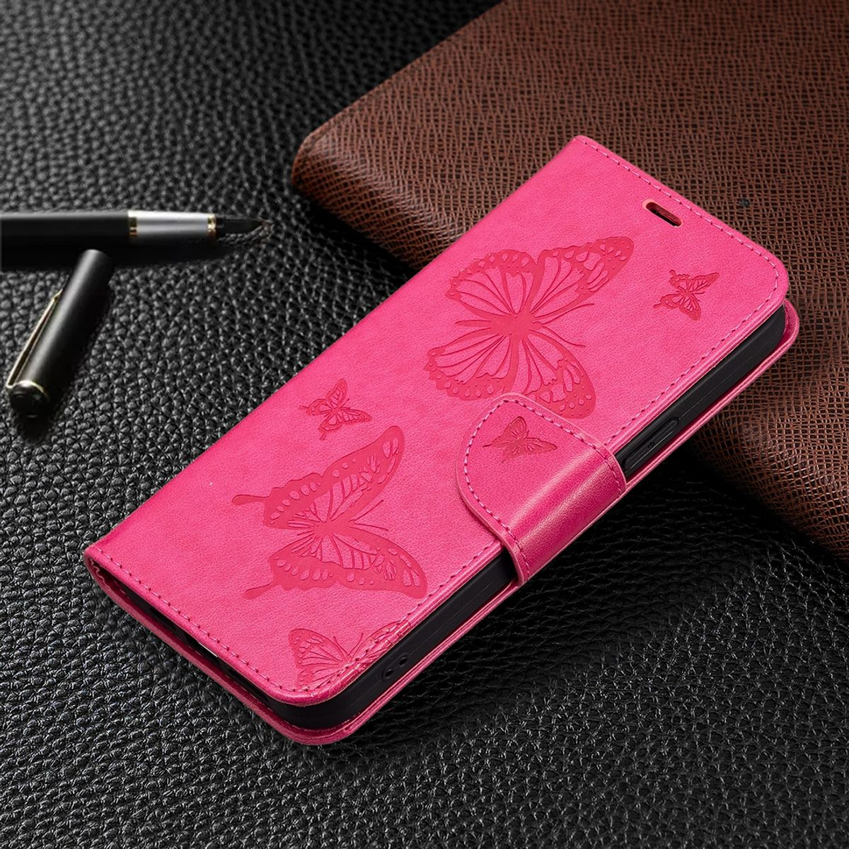 Rosa Handyhülle mit Schmetterlingsdesign. Die Hülle ist geschlossen und zeigt Schmetterlinge. Schwarzer Hintergrund. Stift links.