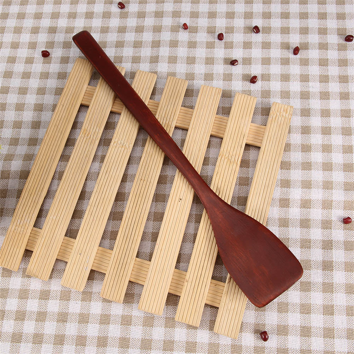 Holzspatel auf einem Holzständer mit roten Bohnen verstreut auf einem karierten Tuch.