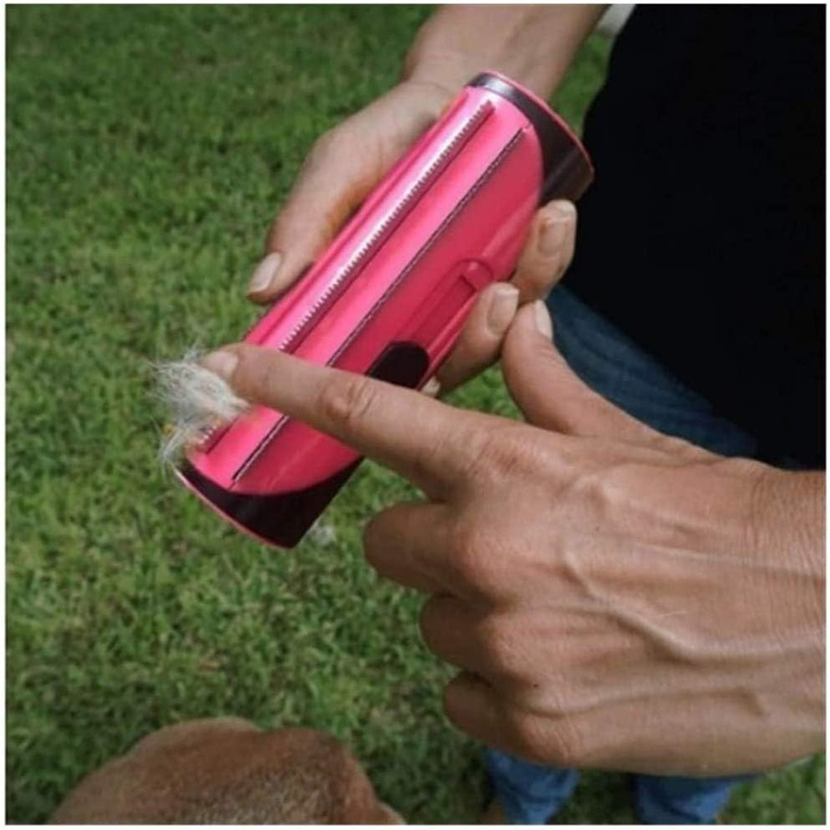Person verwendet einen rosa Tierhaarentferner an einem Hund. Der Hintergrund ist grünes Gras.