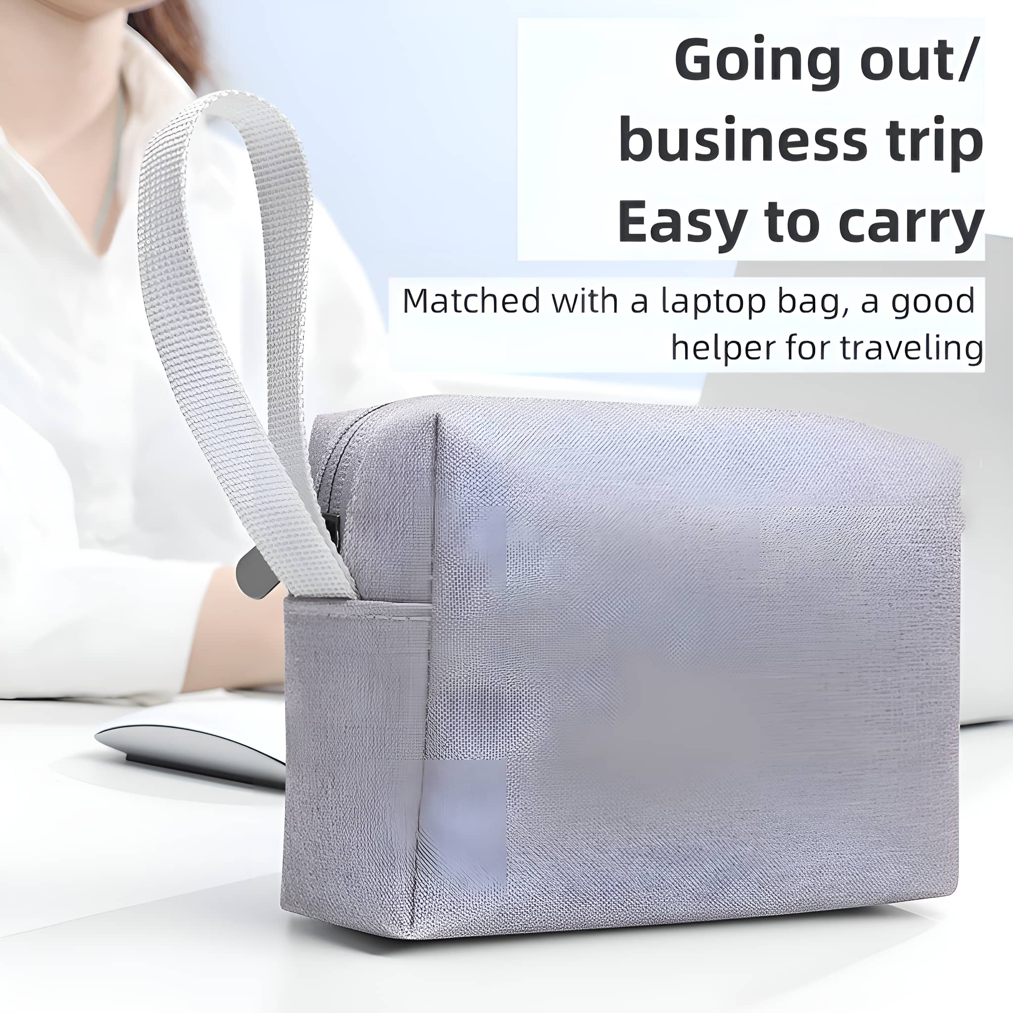 Graue Reisetasche mit weißem Griff. Eine Person ist im verschwommenen Hintergrund in der Nähe eines Laptops.