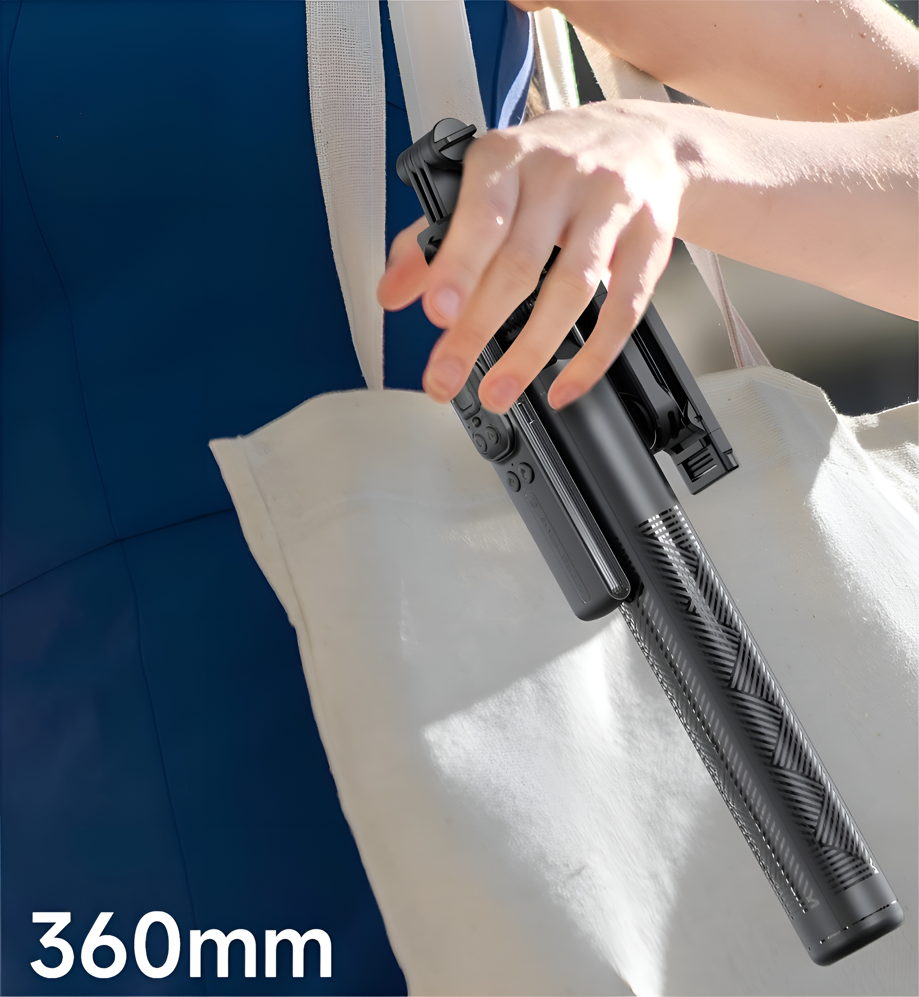 Eine Person hält einen schwarzen Selfie-Stick vor einer weißen Tasche und einem blauen Kleid.