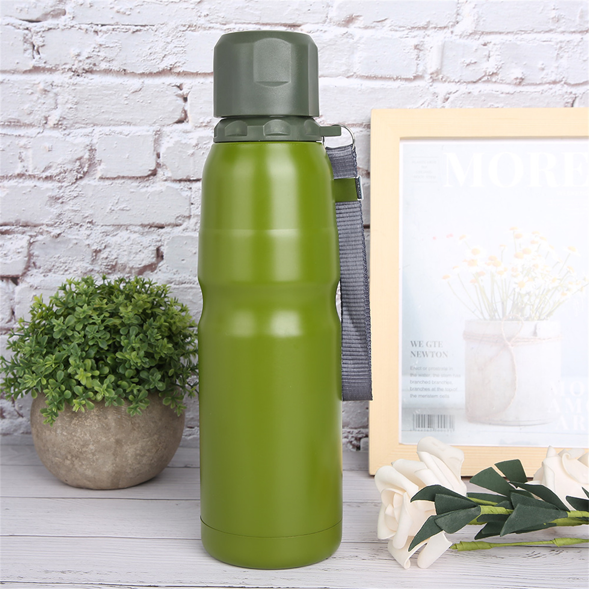 Eine grüne Wasserflasche neben einem weißen gerahmten Bild und einer kleinen Pflanze.