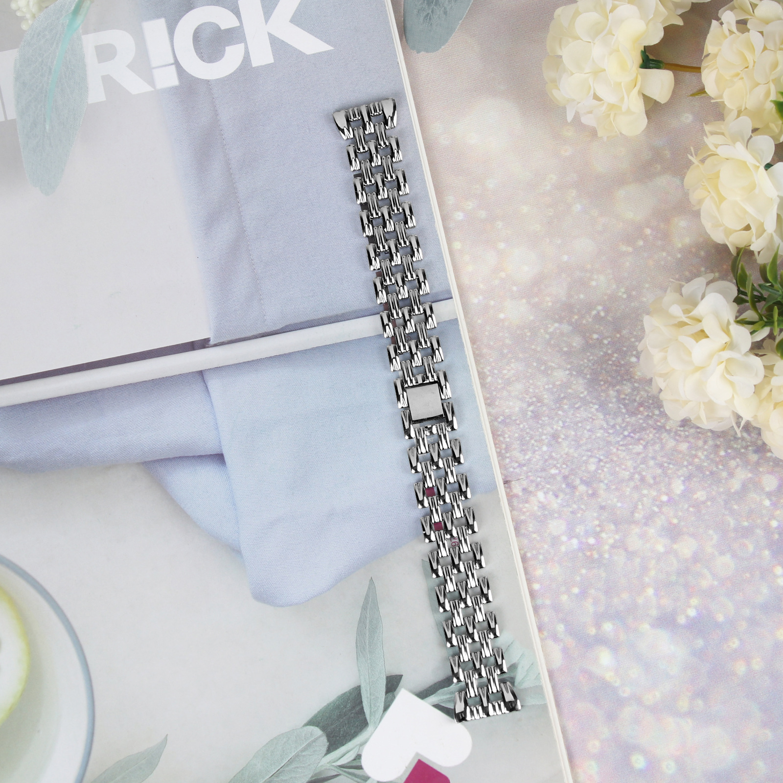 Silbernes Uhrenarmband auf weiß-blauem Hintergrund mit Blumen. Nahaufnahme.