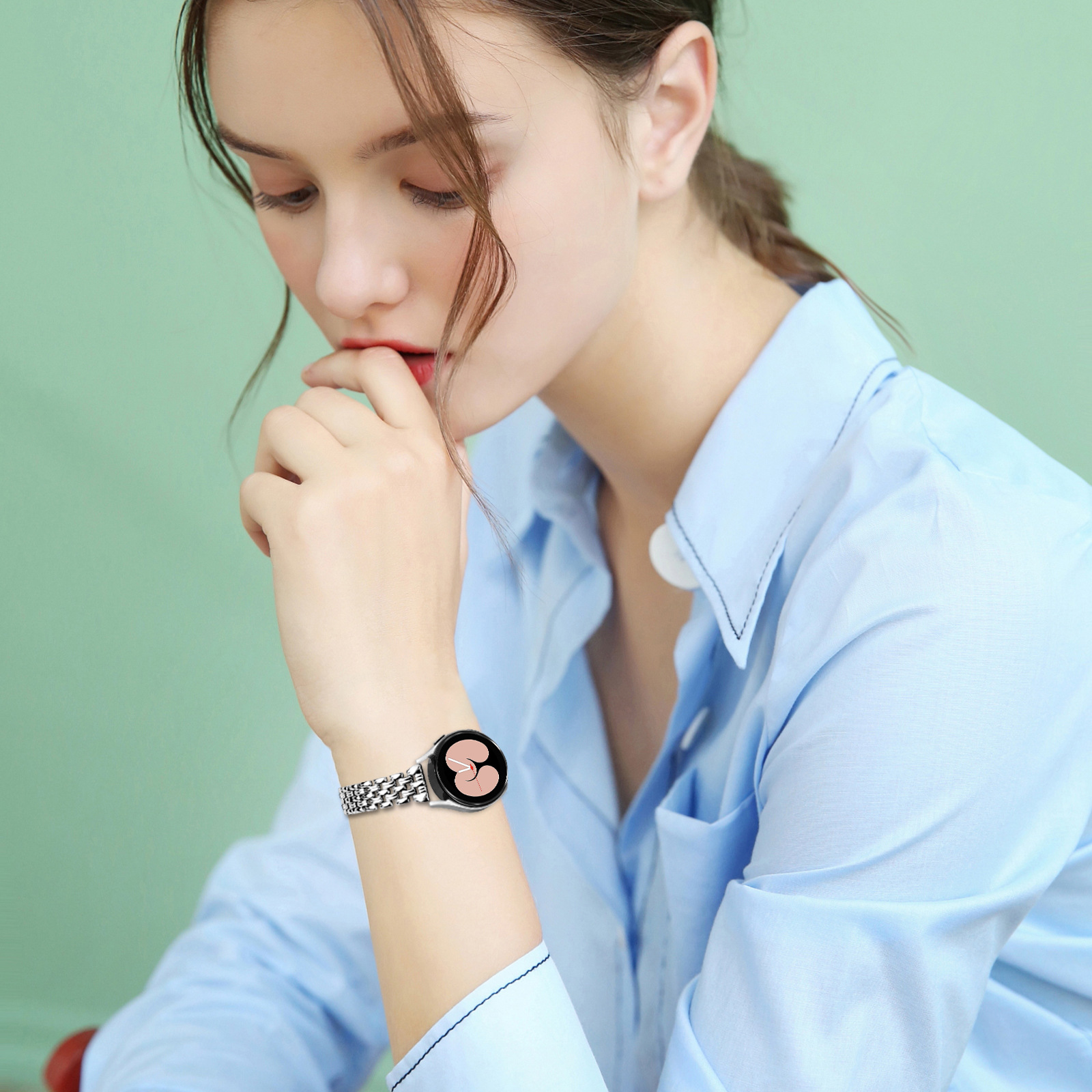 Eine Frau in blauem Hemd zeigt eine silberne Smartwatch mit schwarzem Bildschirm.