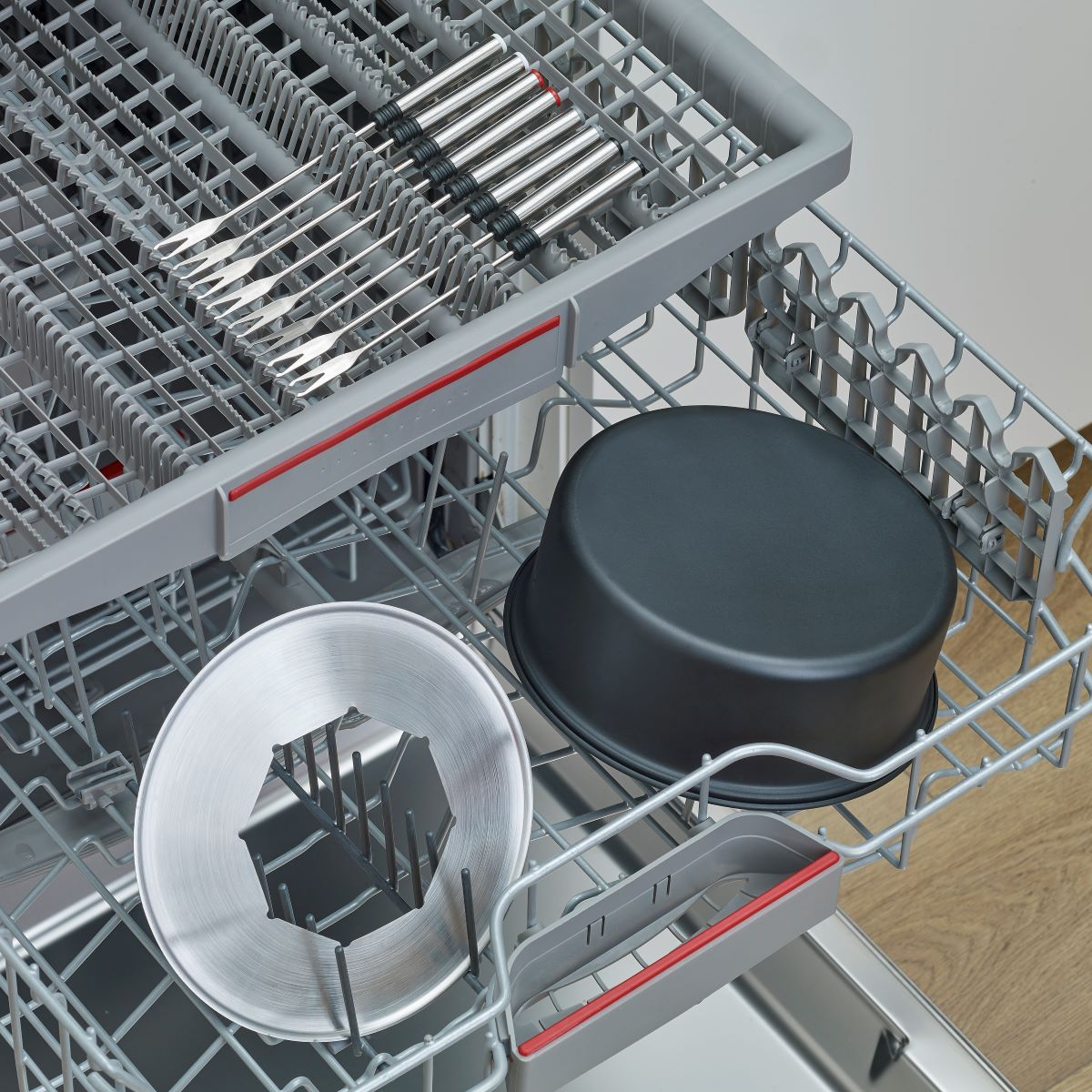 Wnętrze zmywarki z sztućcami, formą do ciasta i innymi naczyniami.
