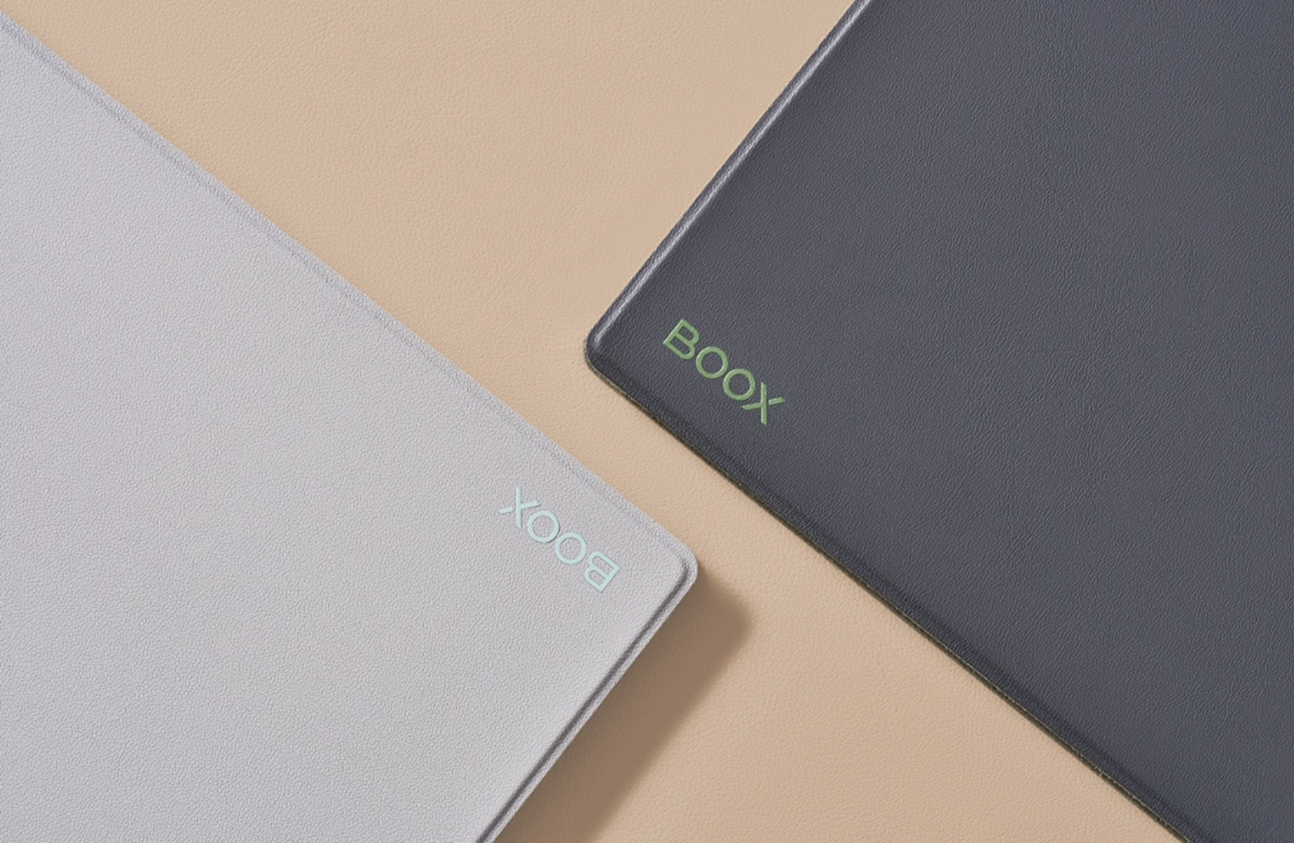 Dos lectores electrónicos BOOX grises y blancos, colocados en diagonal sobre una superficie beige. El texto BOOX es verde.