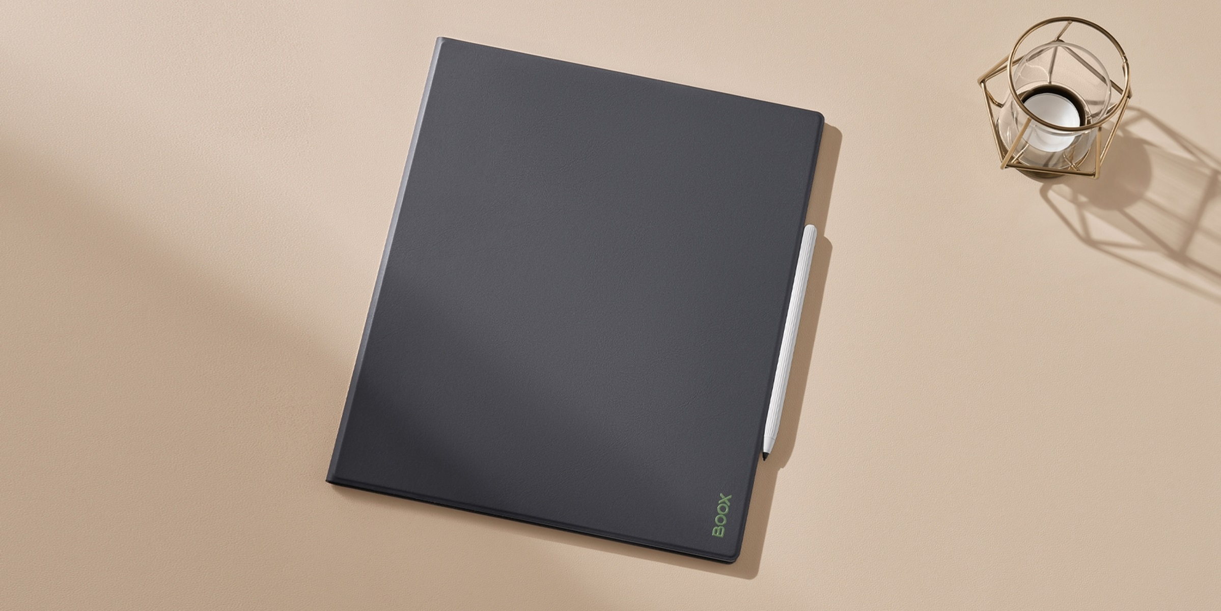 Una tableta negra con un lápiz blanco descansa sobre una superficie beige, decoración dorada a la derecha.