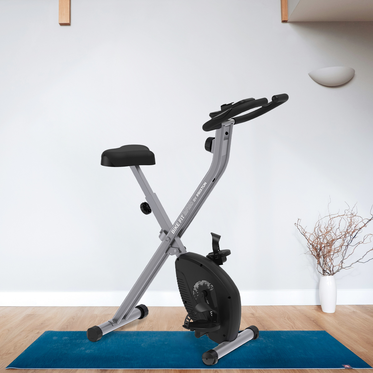 Rower treningowy w pokoju z niebieską matą, białą ścianą i wazonem z suszonymi roślinami. Obecne światło słoneczne.